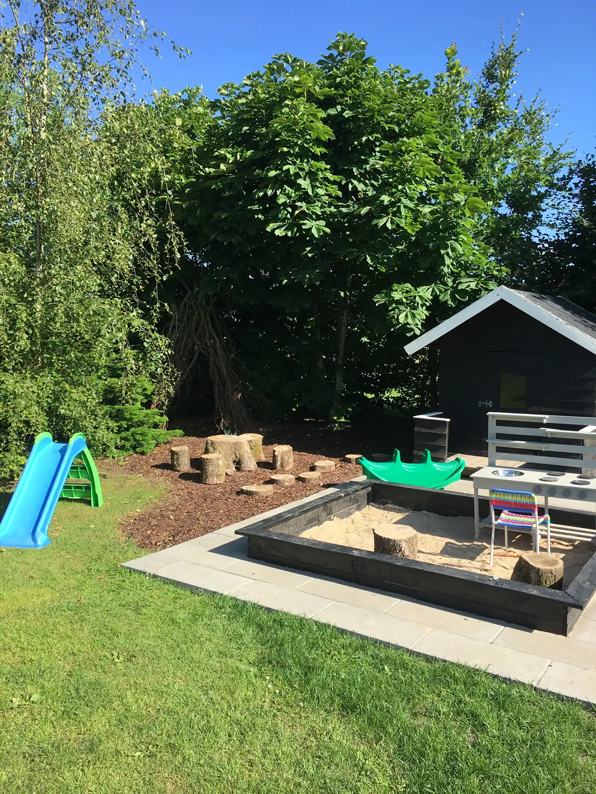 Have med tr&aelig;er, stor sandkasse, hytte, legeting og plads med tr&aelig;stubbe