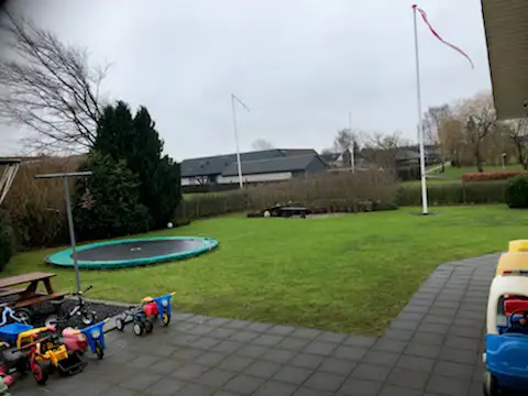 Terrasse og have med trampolin, sm&aring; legecykler og legebiler 